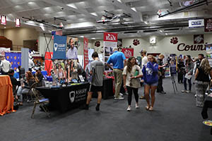 People at booths in large auditorium.